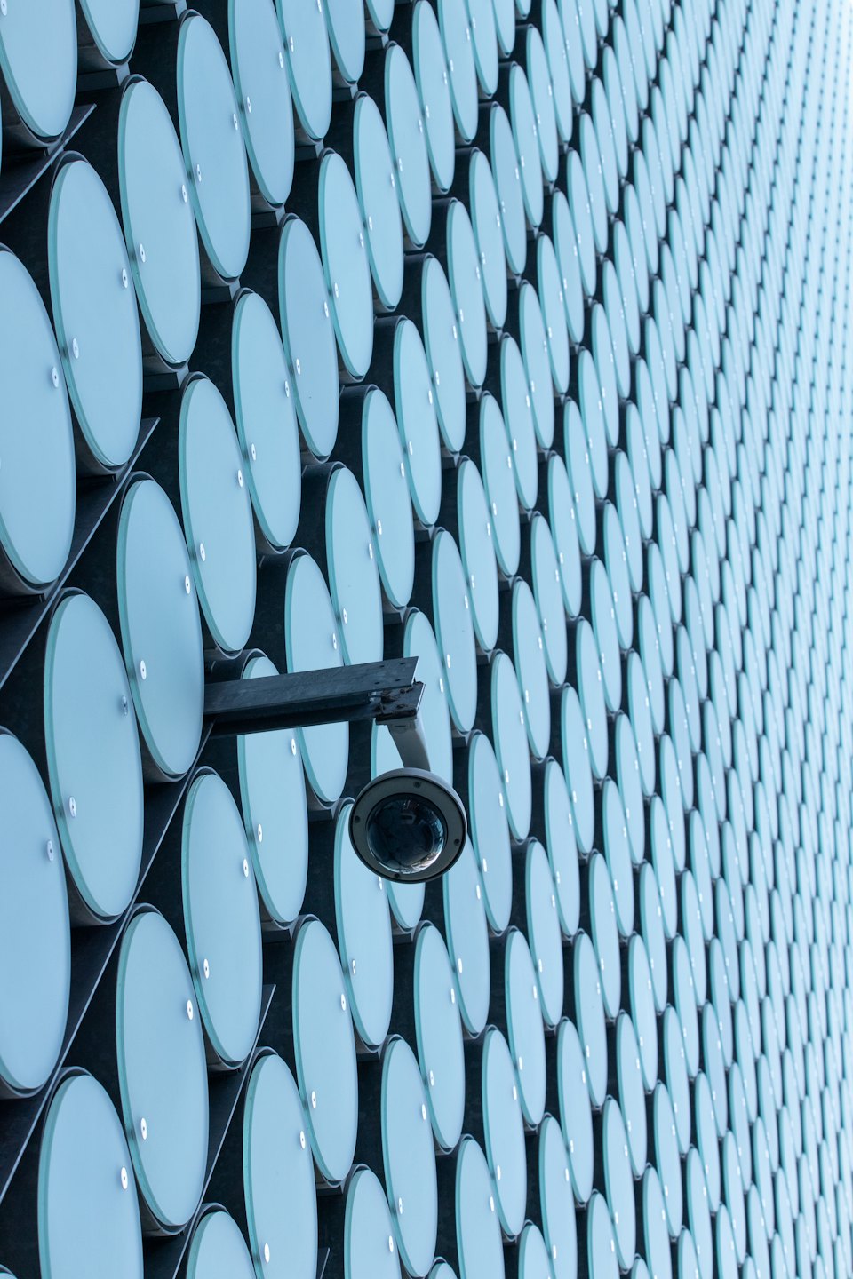 Cámara de seguridad montada en la fachada de un edificio con paneles circulares azules.